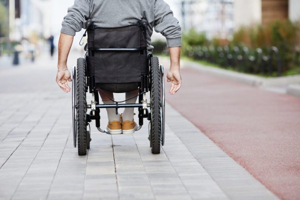 Man in wheelchair riding outdoors Rear view of mature man riding in wheelchair along the street
